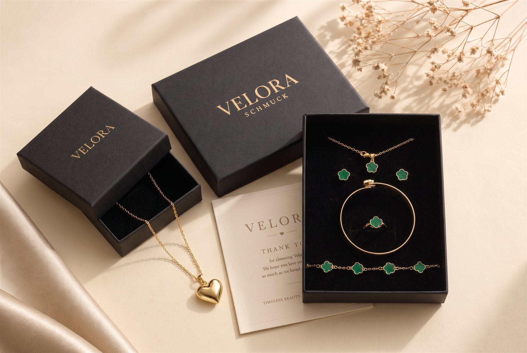 Zwei schwarze VELORA Geschenkboxen mit Herzkette und grünem Kleeblatt Schmuckset, daneben die Dankeskarte
